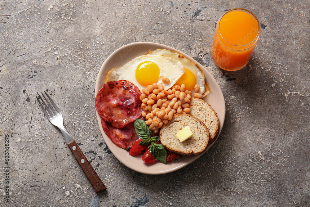 Plate with tasty English breakfast and glass of juice on grey background