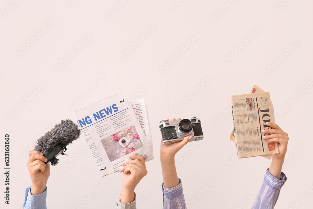 Female hands with newspapers, photo camera and microphone on light background