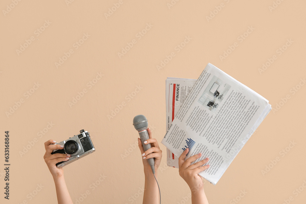 Female hands with photo camera, microphone and newspapers on color background