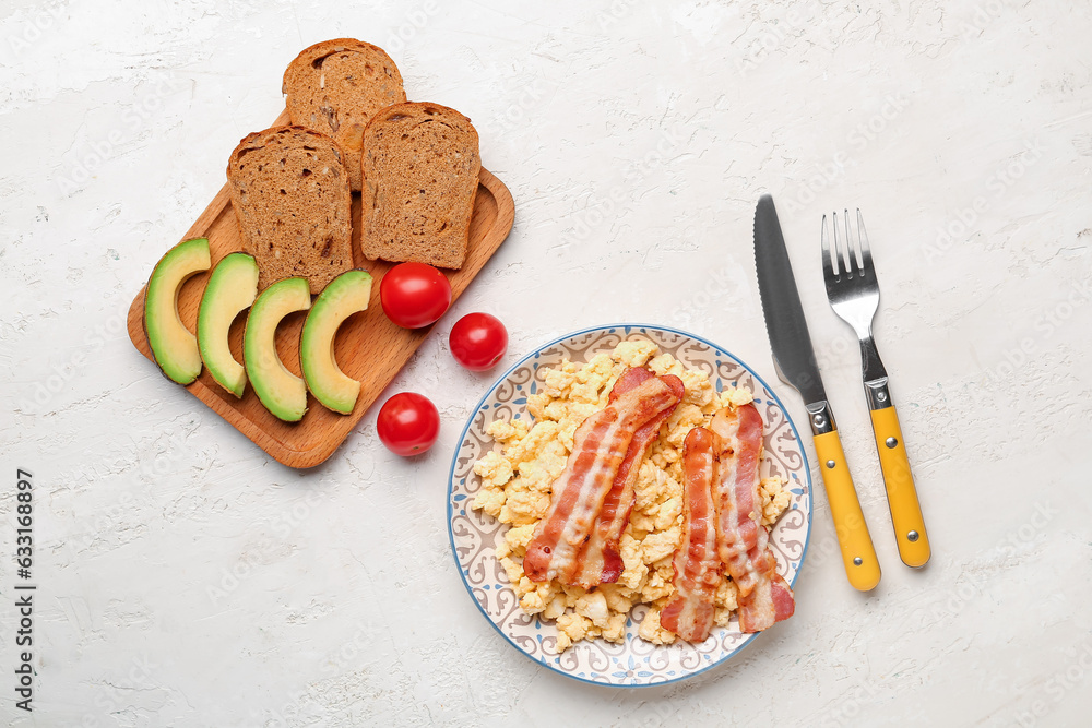 Plate of tasty scrambled eggs with avocado and bacon on light background