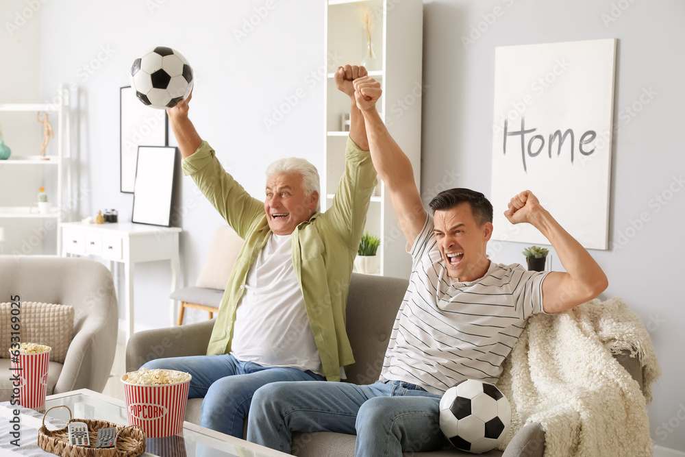 Happy young man with his father watching football game at home