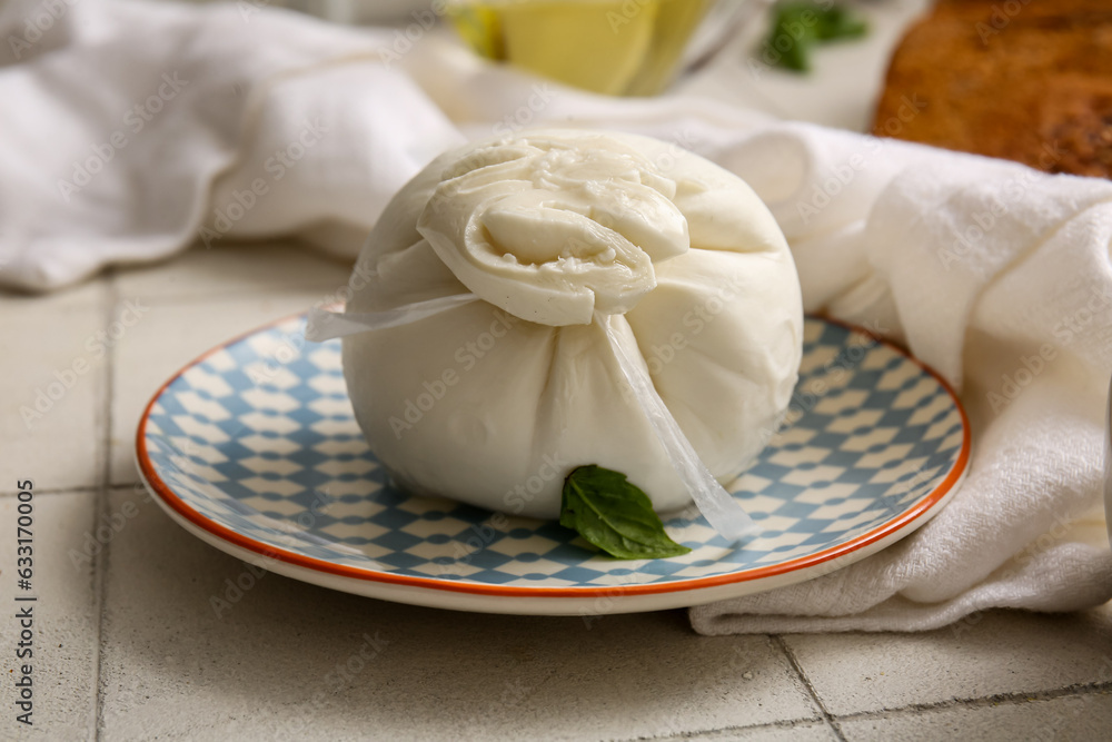 Plate of tasty Burrata cheese with basil on white tile background