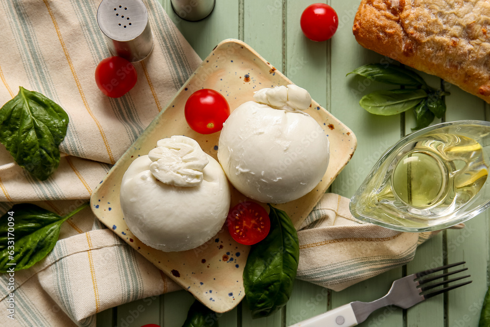 Plate of tasty Burrata cheese with basil and tomatoes on green wooden background