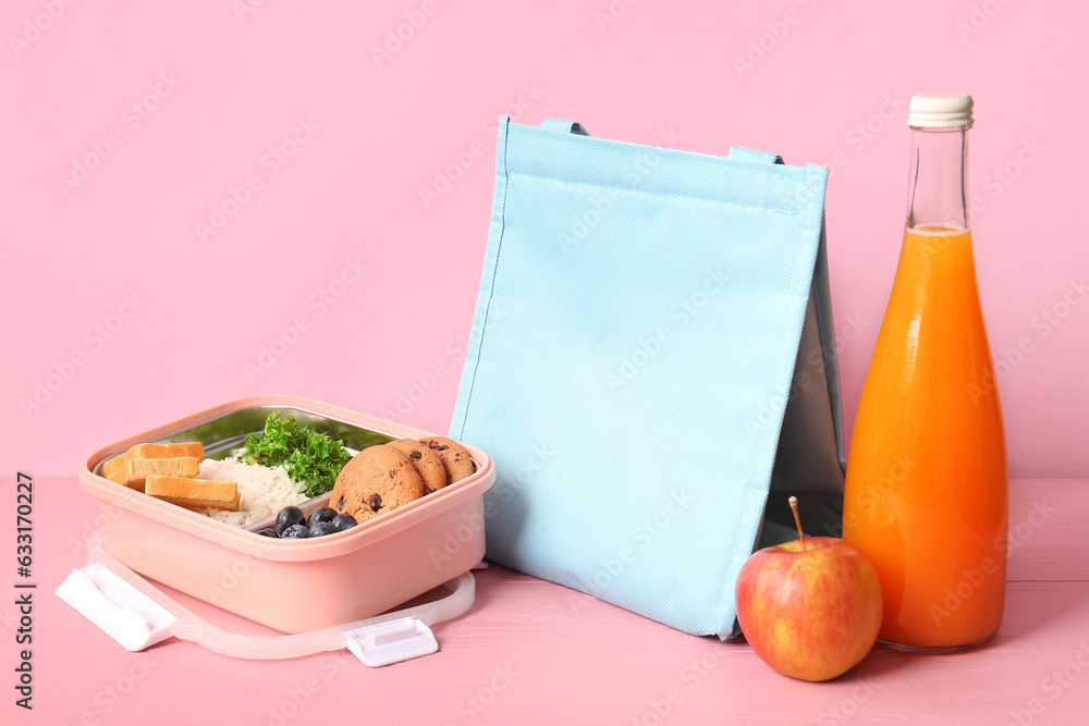 Bag, lunchbox with delicious food and bottle of juice on pink wooden table near wall