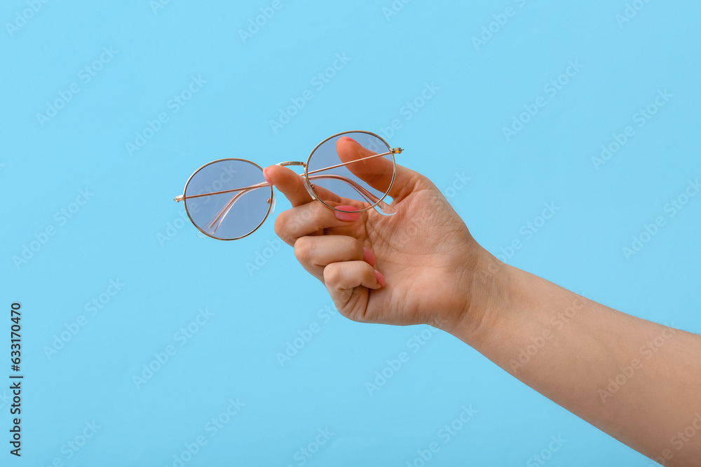 Woman holding stylish sunglasses on blue background