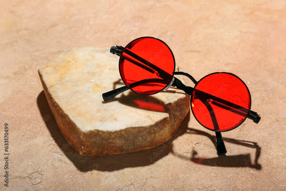 Stone with stylish sunglasses on orange background