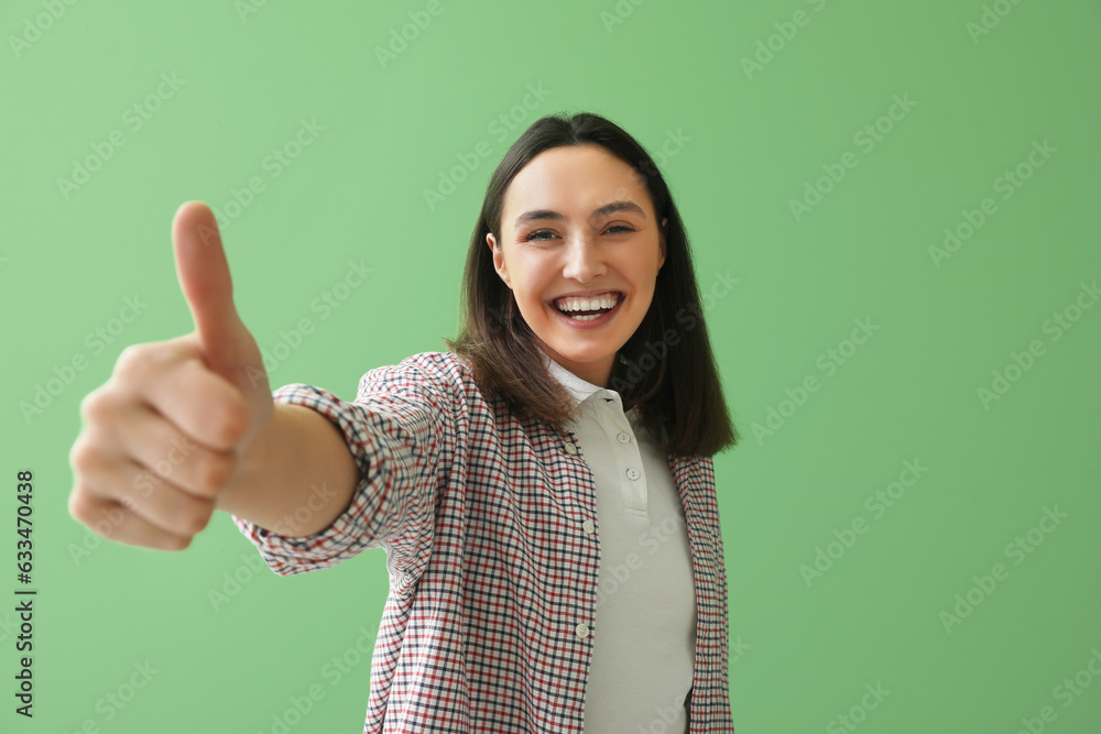 Young woman showing thumb-up on green background