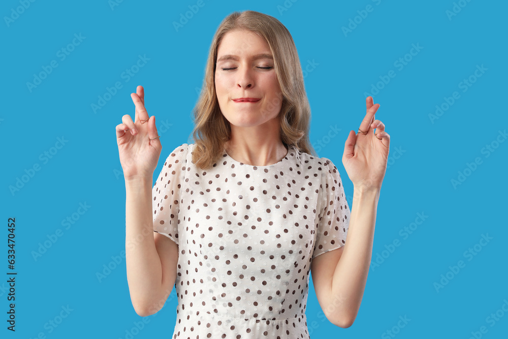 Young woman crossing fingers on blue background