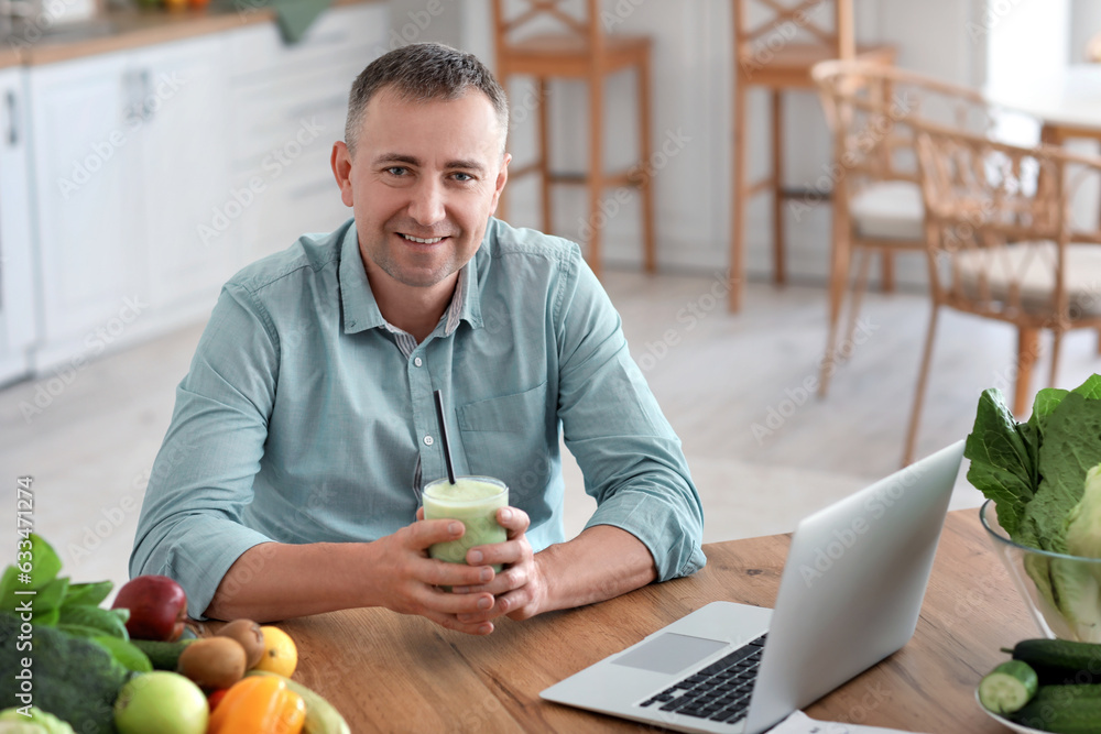 Mature man with glass of fresh vegetable smoothie in kitchen