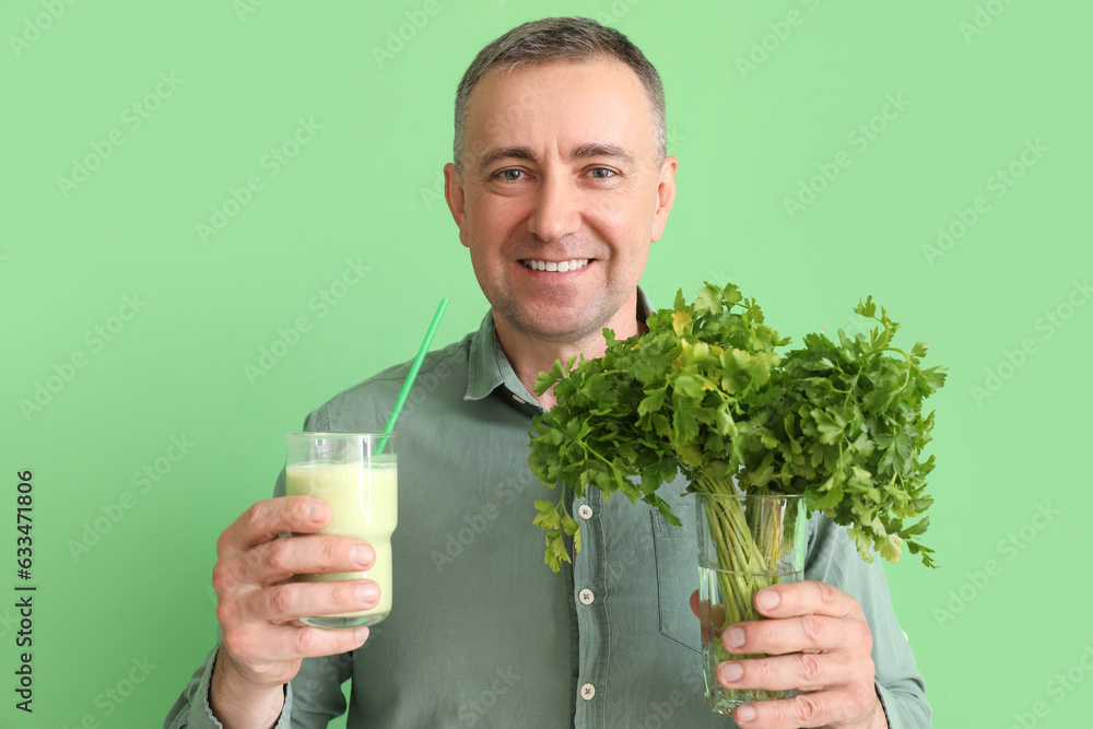 Mature man with glass of vegetable smoothie and parsley on green background, closeup