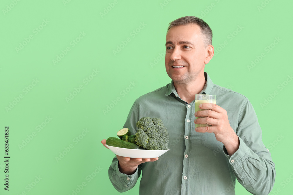 Mature man with glass of smoothie and vegetables on green background