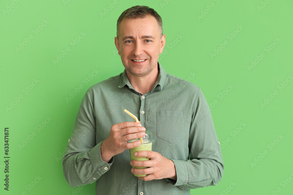 Mature man with glass of vegetable smoothie on green background