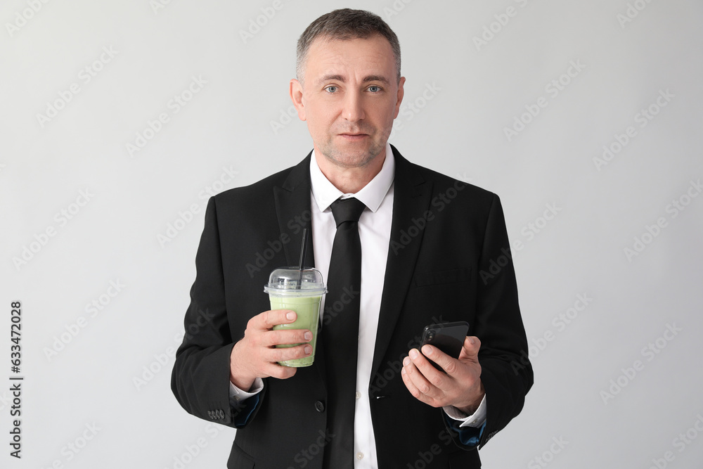 Mature businessman with glass of vegetable smoothie and mobile phone on light background