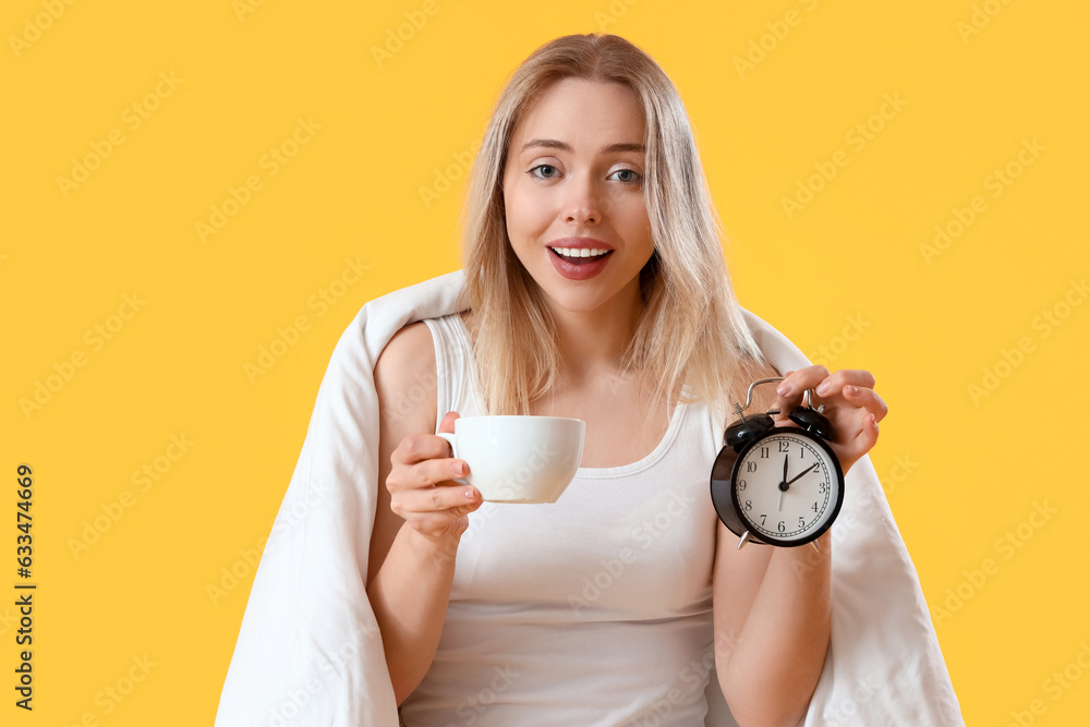 Young woman with alarm clock and cup of coffee on yellow background