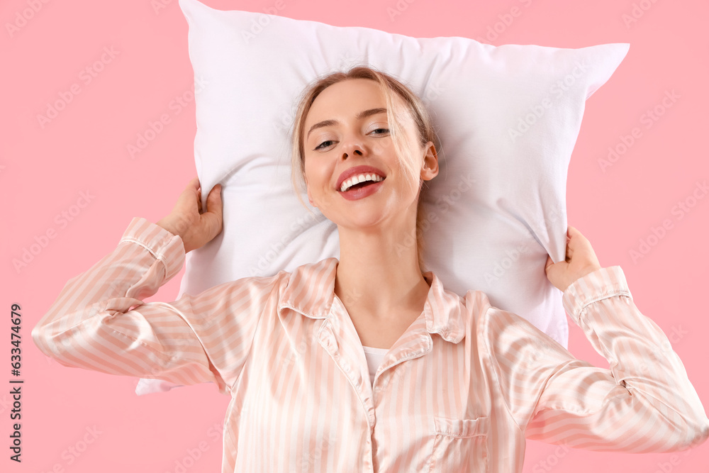 Young woman in pajamas with pillow on pink background