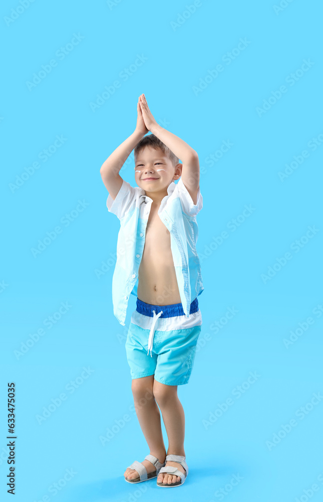 Happy little boy with sunscreen cream on his face against blue background