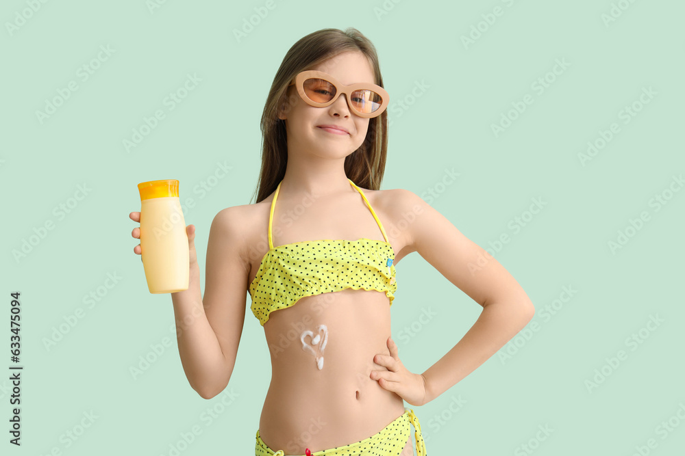 Little girl with sunglasses and bottle of sunscreen cream on pale green background