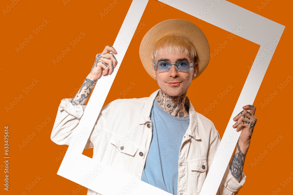 Young tattooed man in stylish sunglasses with frame on color background