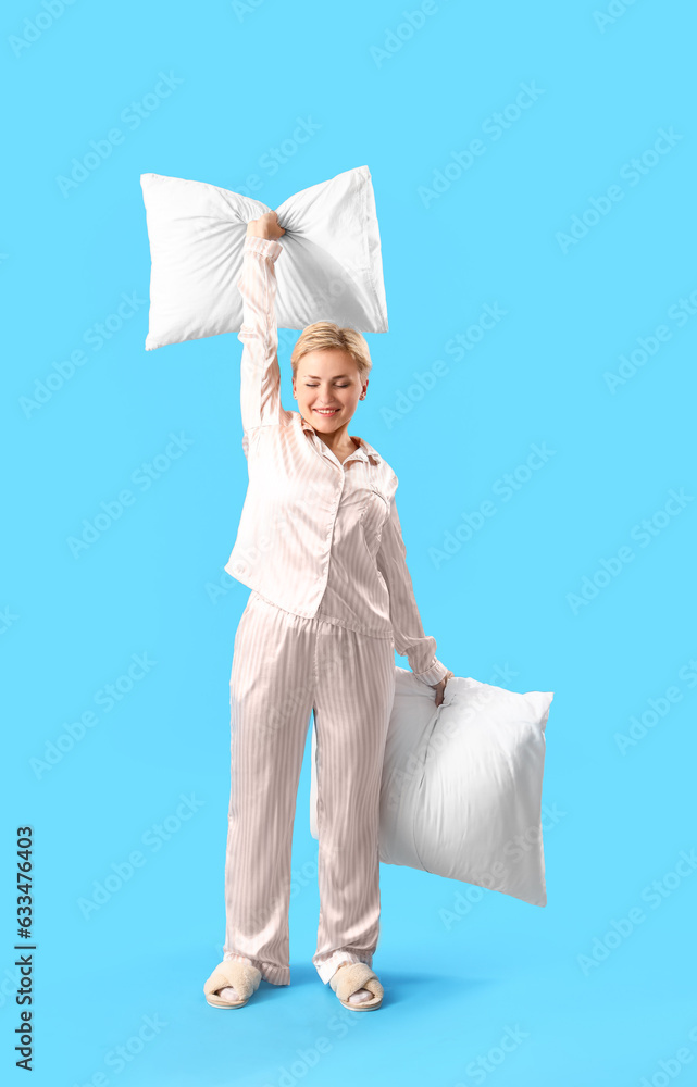 Young woman in pajamas with pillows on blue background