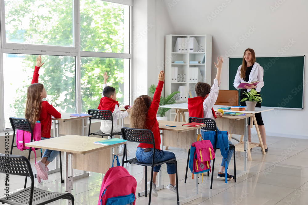 Little pupils raising hands during lesson at school