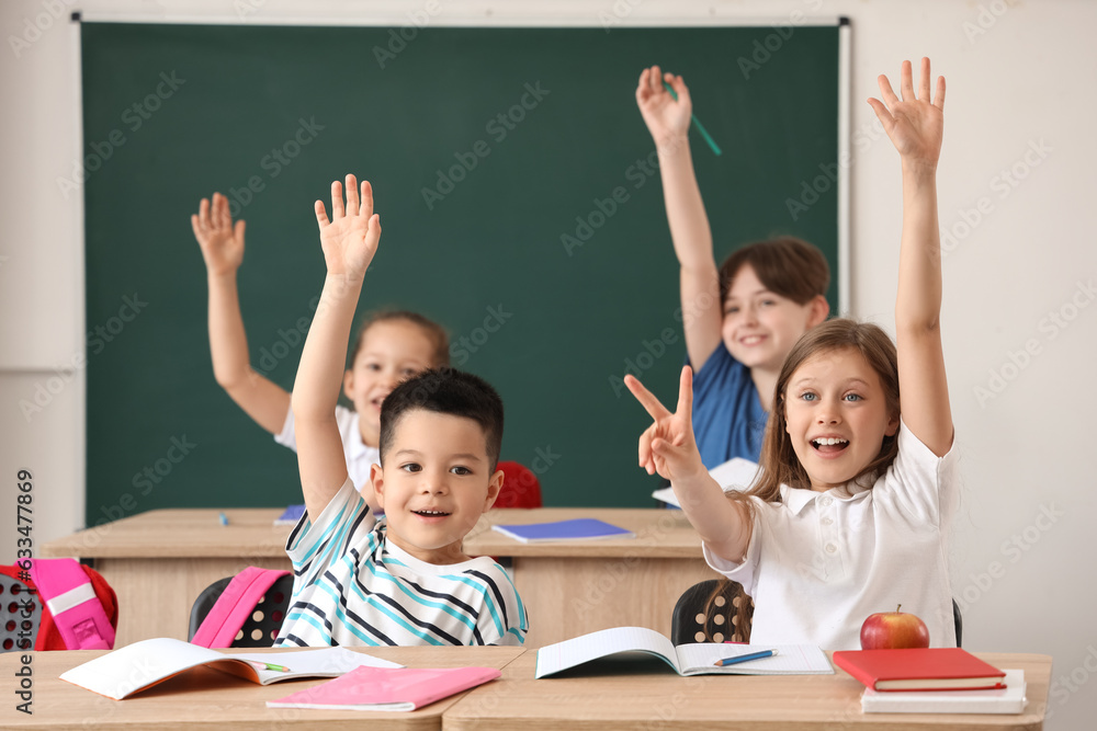 Little pupils raising hands during lesson in classroom