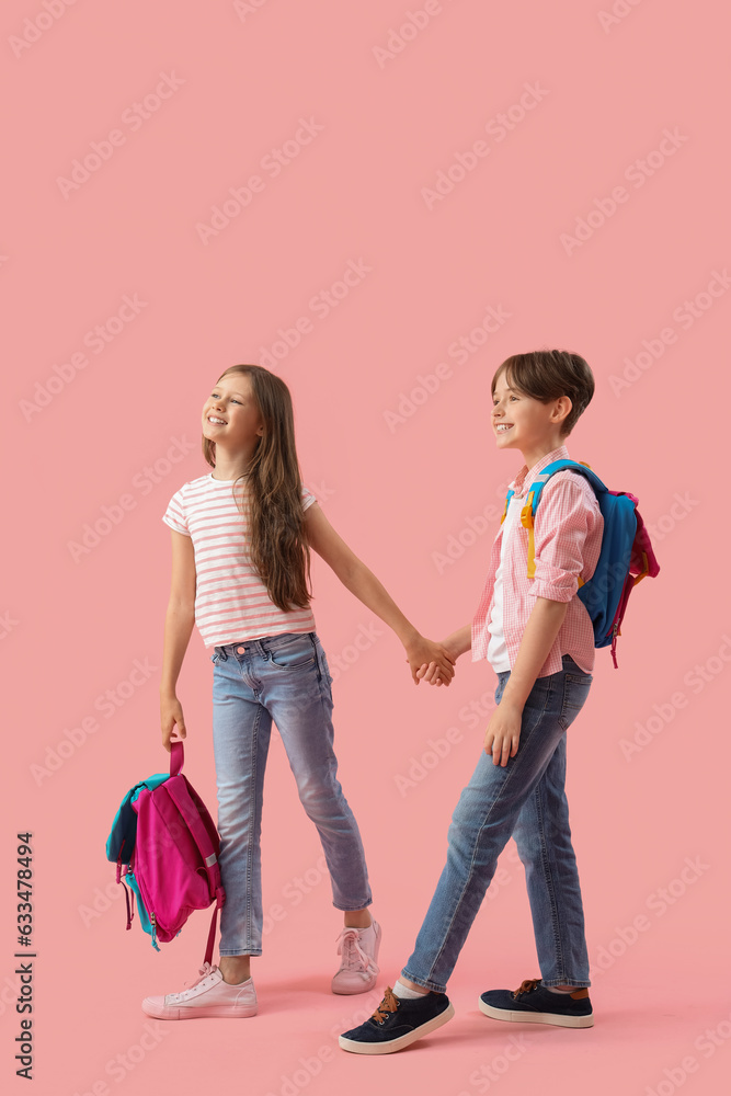 Little pupils with backpacks holding hands on pink background