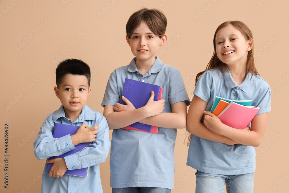 Little pupils with copybooks on beige background