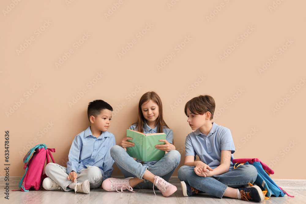 Little pupils reading book near beige wall