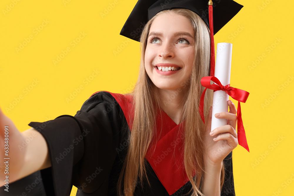 Female graduate student with diploma taking selfie on yellow background, closeup