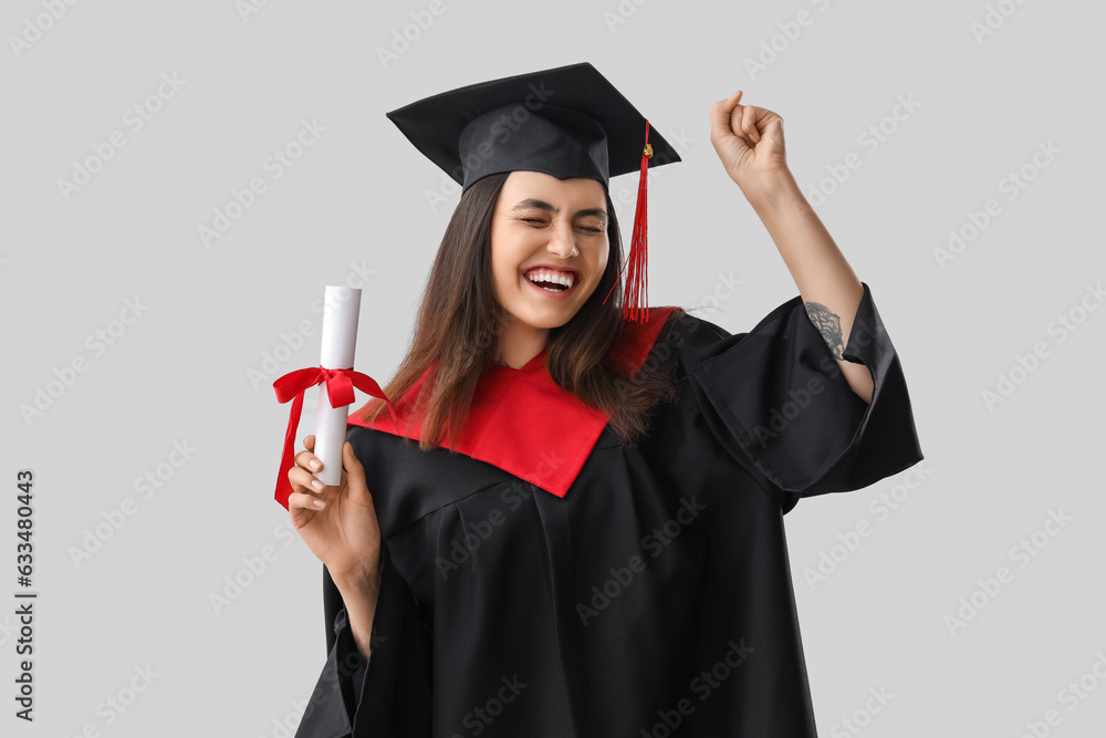 Happy female graduate student with diploma on light background