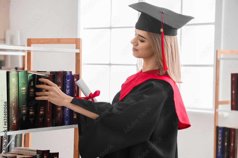 Female graduate student with diploma taking book from shelf in library