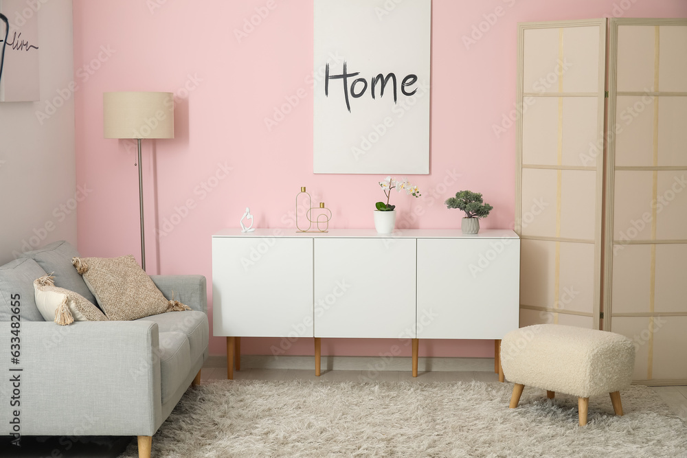 Interior of living room with cozy grey sofa, white cabinet and poster