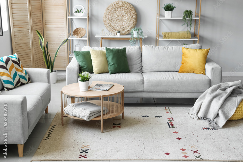 Cozy grey sofas, coffee table and pouf with soft blanket in interior of living room