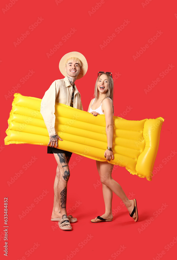 Young couple with inflatable mattress on red background