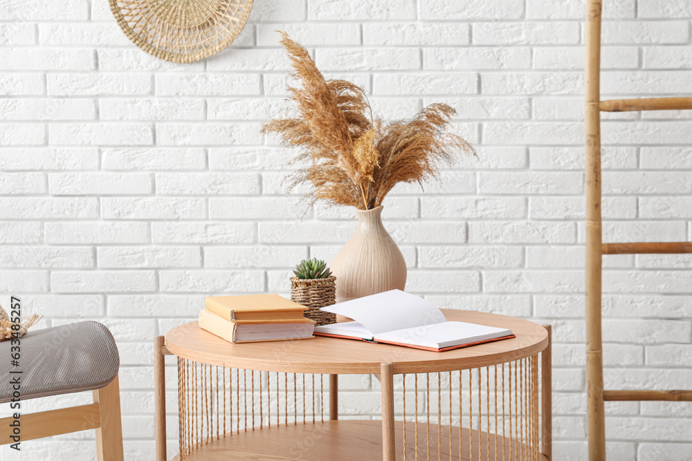 Light wooden coffee table with vase of dried pampas grass and ladder near white brick wall