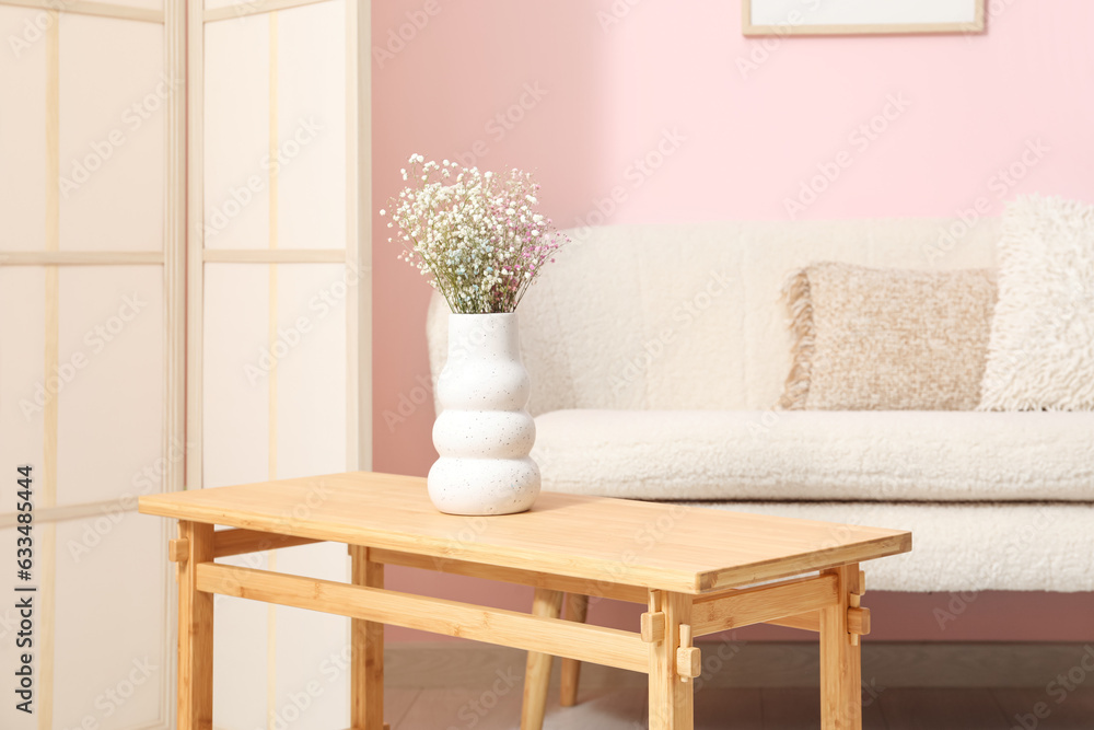 Light wooden coffee table with sofa and dressing screen near pink wall