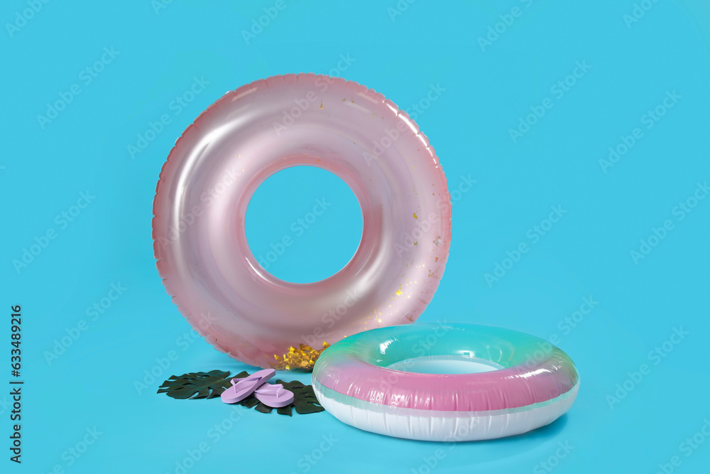 Inflatable rings with flip-flops and palm leaves on blue background