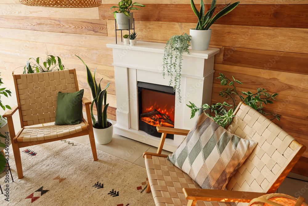 Stylish fireplace and armchairs near wooden wall