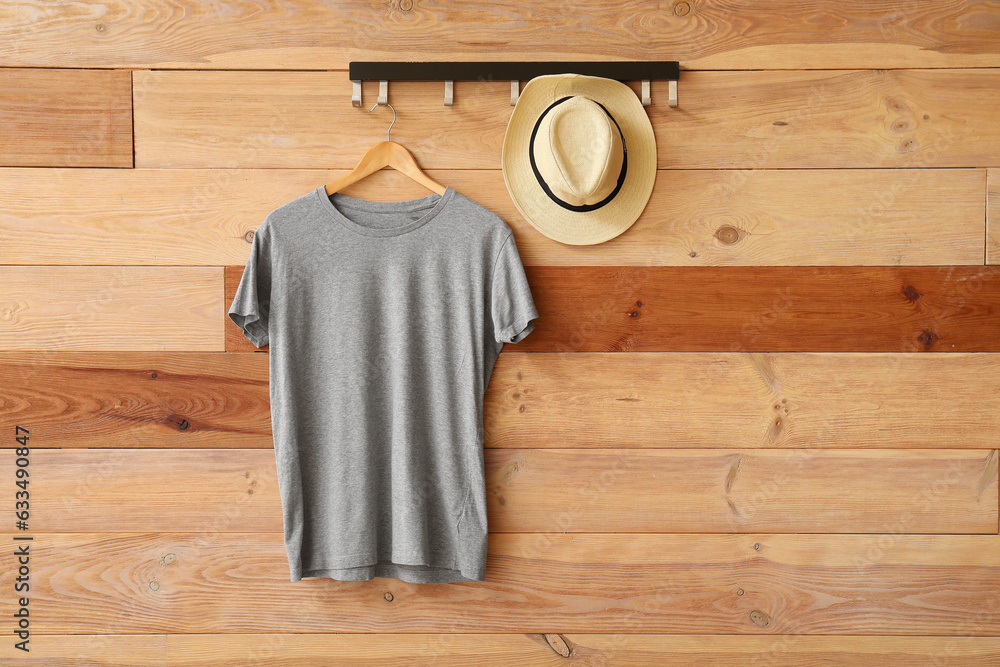 Stylish grey t-shirt and hat hanging on wooden background