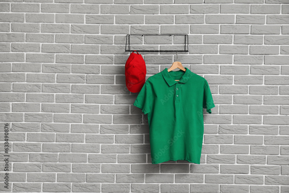 Stylish green t-shirt and cap hanging on grey brick wall