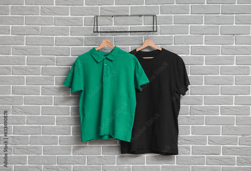 Stylish t-shirts hanging on grey brick wall