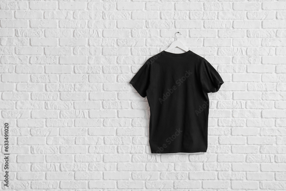 Stylish black t-shirt hanging on white brick wall