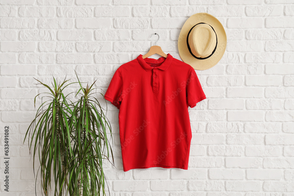 Stylish red t-shirt and hat hanging on white brick wall