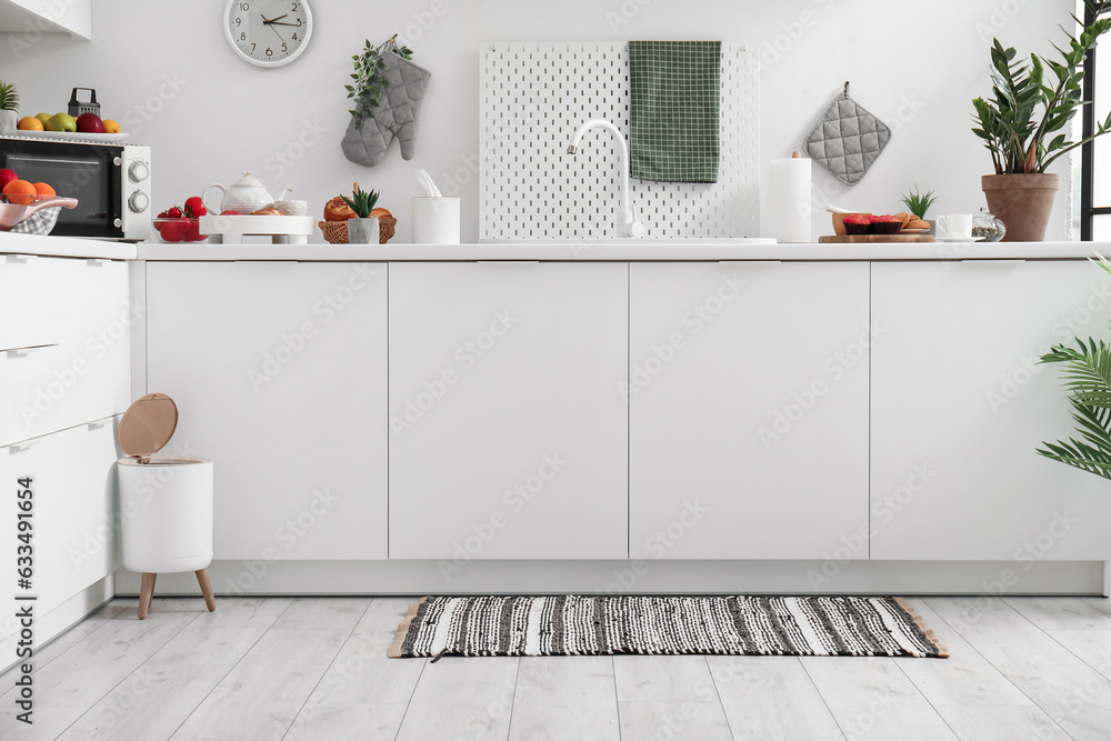 Interior of modern kitchen with stylish rug, trash bin and white counters