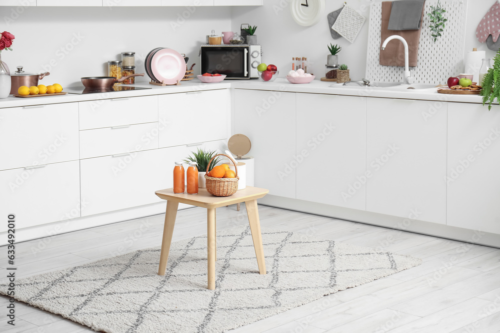 Small table with fruits and juice on stylish rug in modern kitchen