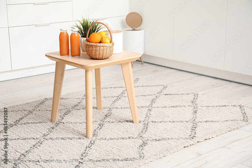 Small table with fruits and juice on stylish rug in modern kitchen