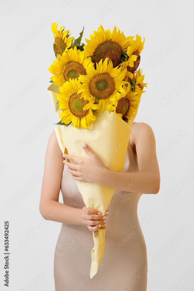 Woman holding bouquet of beautiful sunflowers in paper on light background