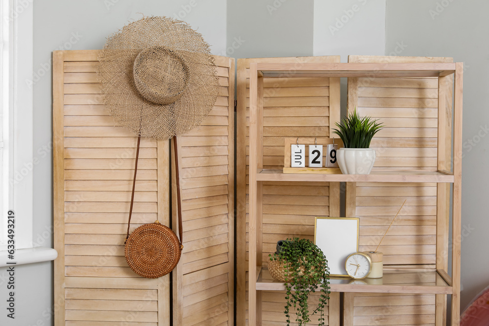 Shelf unit with decor and beach accessories near wooden folding screen in room