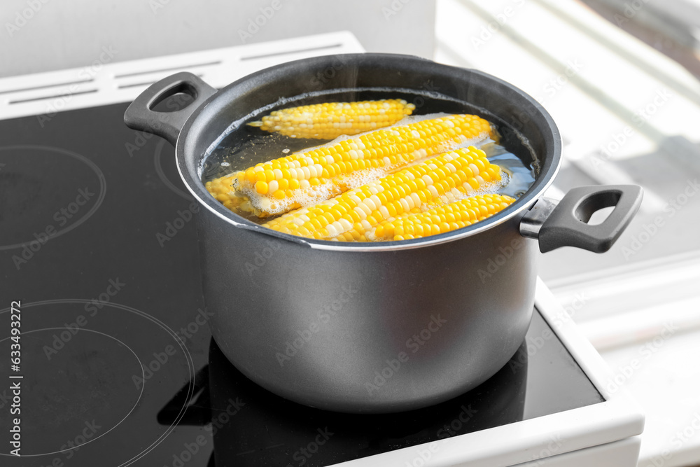 Cooking pot with boiling corn cobs on electric stove in kitchen