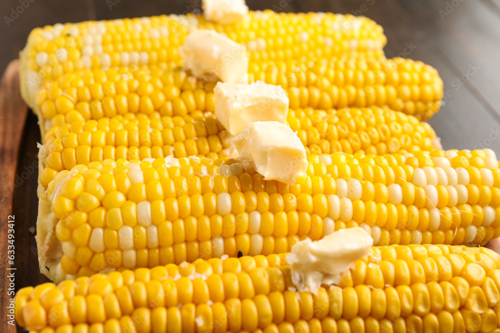 Board of boiled corn cobs with butter on wooden background